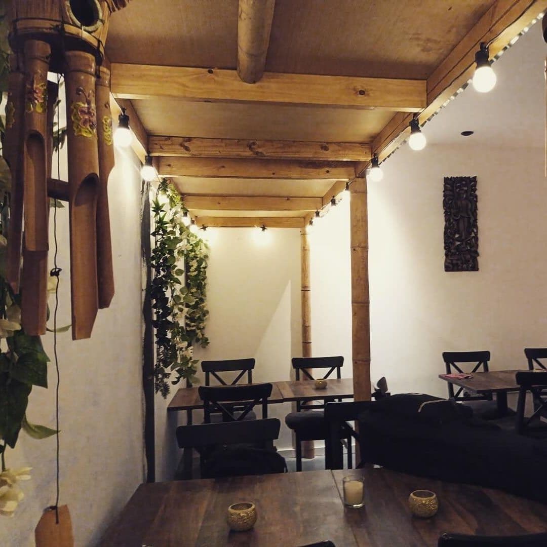 The Old Kings Arms cozy interior wooden beams string lights Cozy interior of The Old Kings Arms with wooden beams, string lights, and greenery, featuring simple wooden tables and chairs.