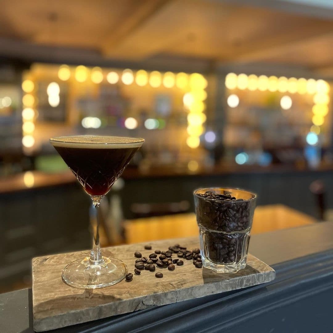 The White Swan Espresso Martini Coffee Beans Bar Ambiance Espresso martini and coffee beans on a marble tray at The White Swan bar, with soft bokeh lighting in the background.