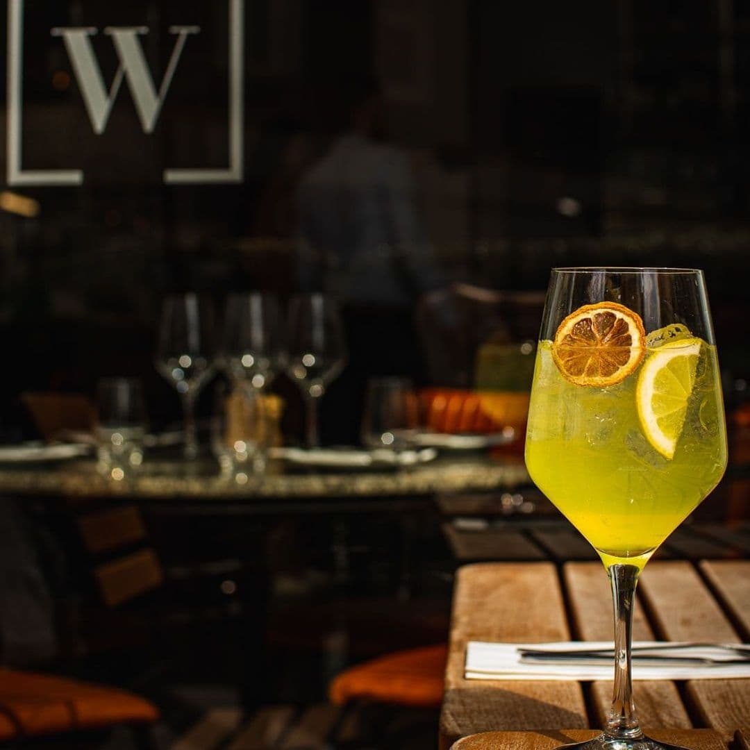 The Whitehall Restaurant Bar Citrus Cocktail Elegant Setting Refreshing cocktail with citrus garnish on a table at The Whitehall Restaurant & Bar, with elegant dining settings in the background.