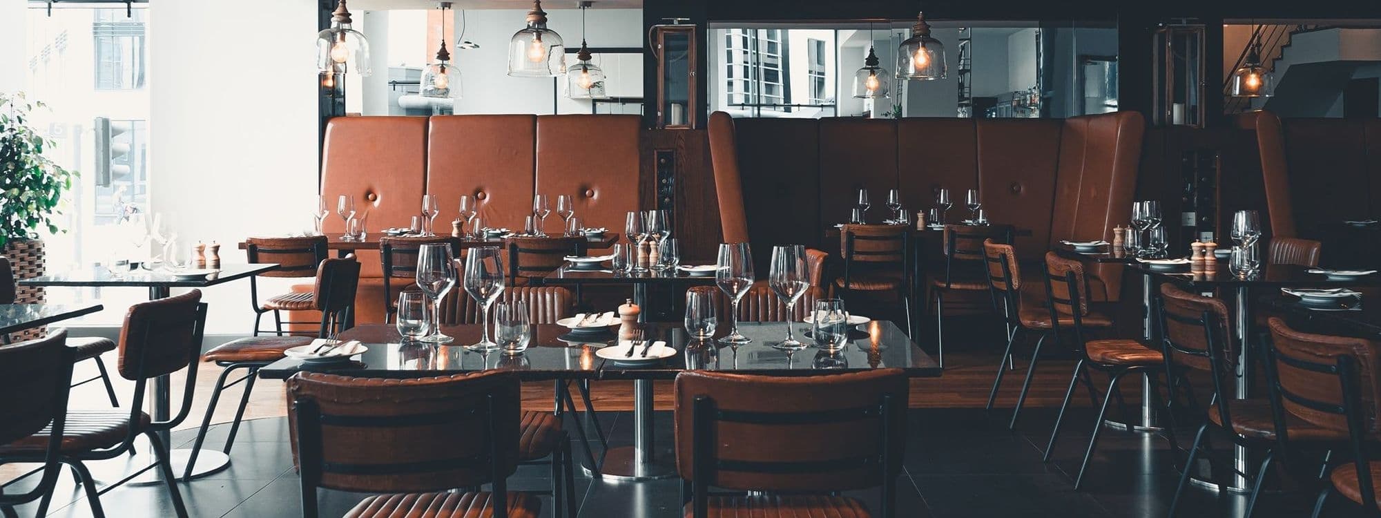 Elegant interior of The Whitehall Restaurant & Bar with neatly arranged dining tables, wine glasses, and leather chairs under warm lighting.