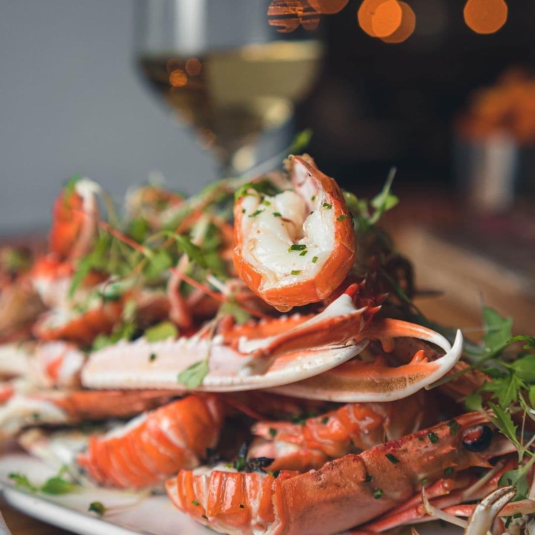 The Whitehall Restaurant Bar Seafood Platter Fine Dining Experience Close-up of a seafood dish featuring succulent shrimp and crab legs garnished with fresh herbs, served at The Whitehall Restaurant & Bar, with a glass of white wine in the background.