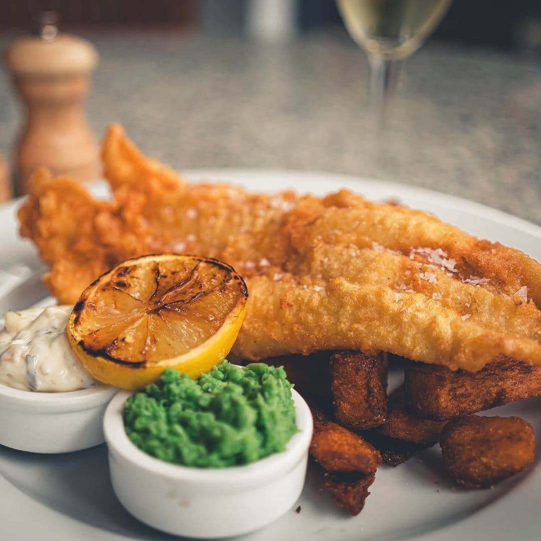 The Whitehall Restaurant & Bar_Gourmet Fish and Chips Platter Golden-battered fish and chips served with mushy peas, tartar sauce, and a grilled lemon slice at The Whitehall Restaurant & Bar.