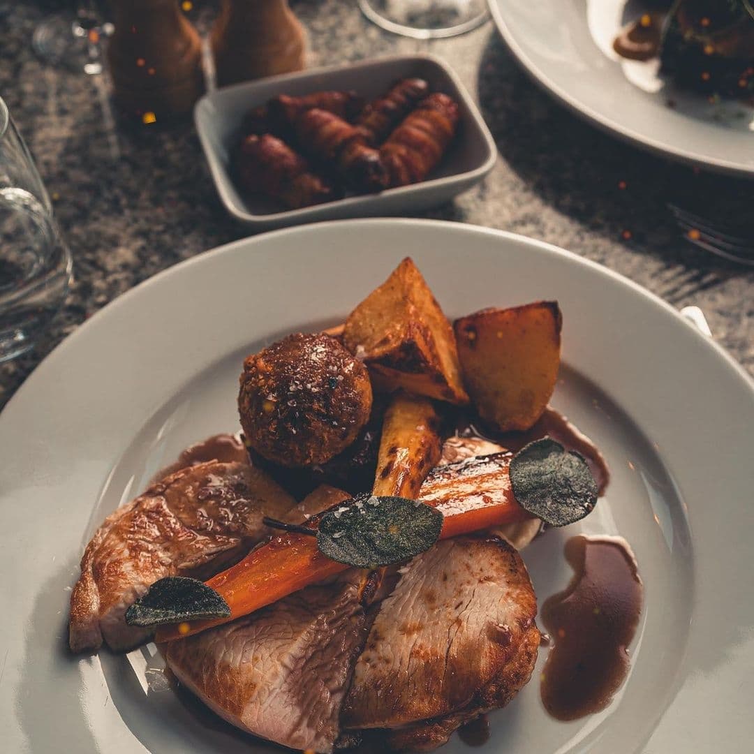 The Whitehall Restaurant & Bar_Gourmet_Roasted_Meal_Plating Gourmet meal at The Whitehall Restaurant & Bar featuring roasted meat slices, carrots, potatoes, and a garnish, served on a white plate with a warm, inviting ambiance.