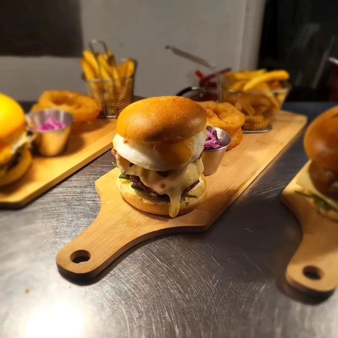 Three_Horse_Shoes_Oulton_Gourmet_Burger_Presentation Gourmet burgers served on wooden boards with sides of fries and onion rings at Three Horse Shoes Oulton.