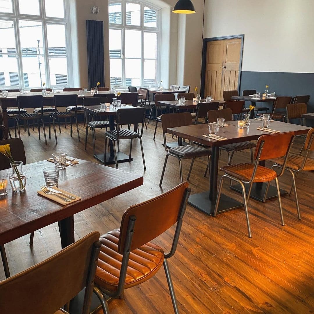 Threes A Crowd_elegant dining interior wooden furniture Interior of Three’s A Crowd restaurant with wooden flooring, arranged dining tables and chairs, and natural light from large windows.