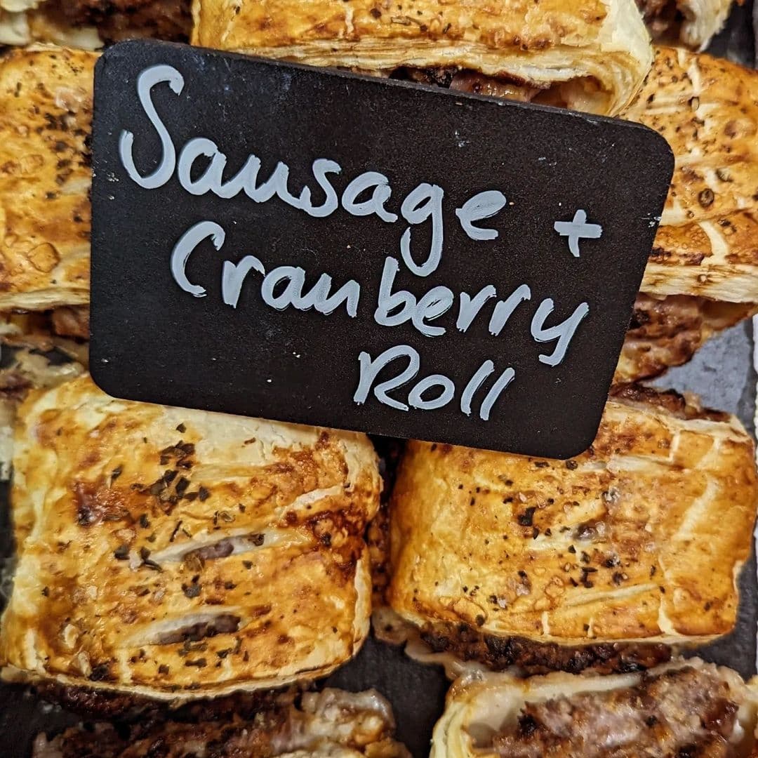 TrulyScrummy_SausageCranberryRoll_DeliciousBakery_Tourism Alt text: "Golden-brown sausage and cranberry rolls on display at Truly Scrummy, with a small black sign indicating the flavor."