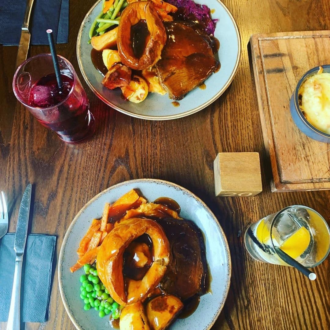 Two Pointers_Gourmet Roast Dinner Traditional Cuisine Traditional British Sunday roast with Yorkshire pudding, vegetables, and gravy at Two Pointers, served on a wooden table with drinks.