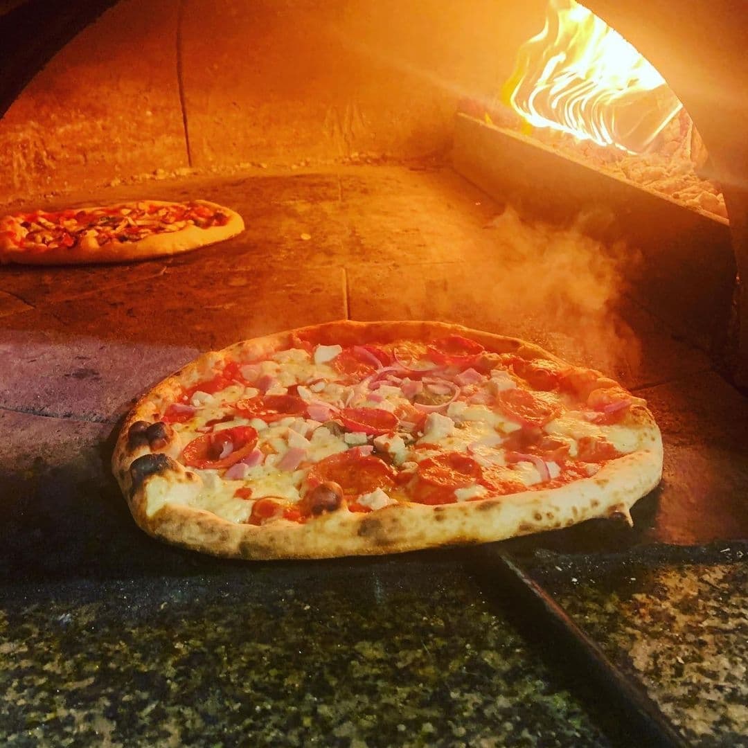 WOOD FIRE DINE Pizzeria Artisan Pizza Brick Oven Flames Freshly baked pizza with toppings inside the brick oven at WOOD FIRE | DINE Pizzeria.