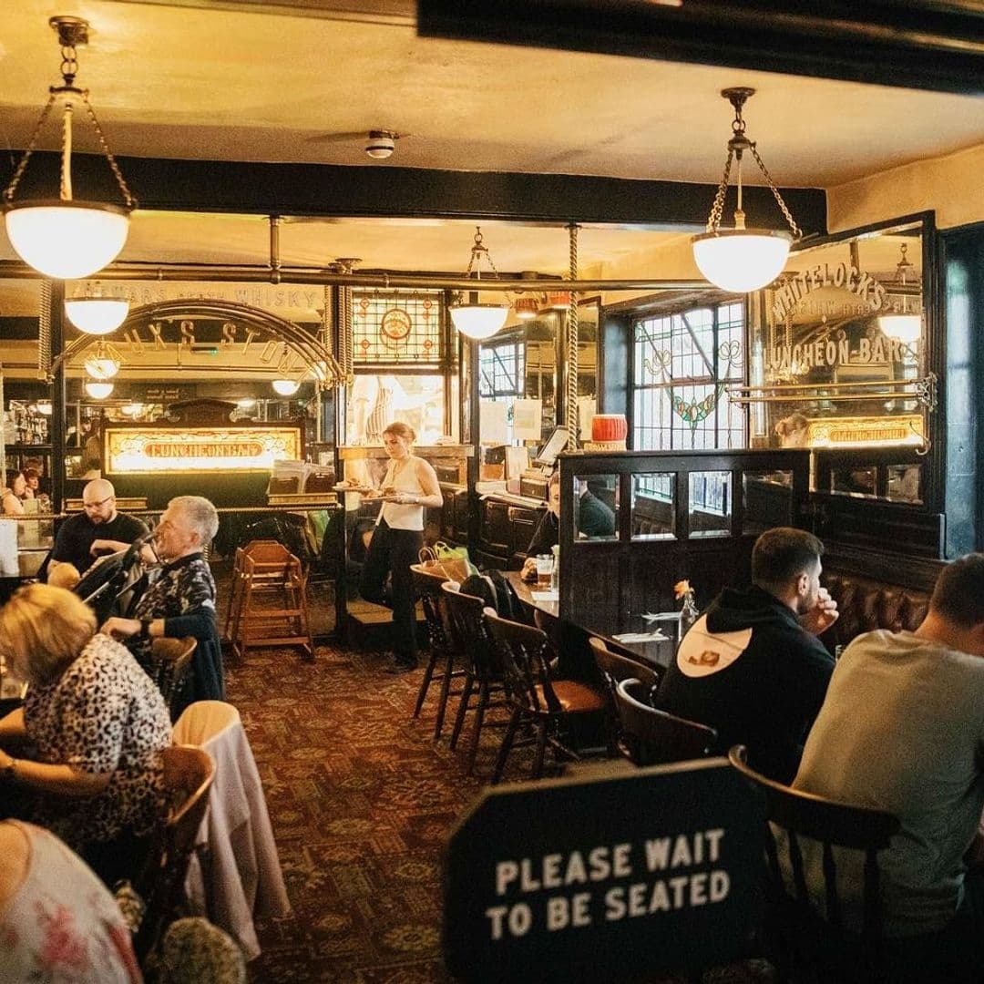 Whitelocks Ale House Vintage Interior Customers Relaxing Interior of Whitelock's Ale House with patrons seated at tables, vintage decor, and a "Please Wait to be Seated" sign in the foreground.