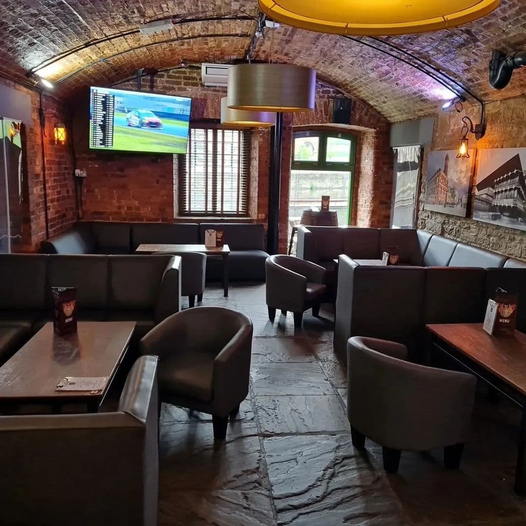 Aire_Bar_Cozy_Interior_Brick_Walls_Comfortable_Seating Interior of Aire Bar with exposed brick walls, leather seating, and a television displaying a sports match.