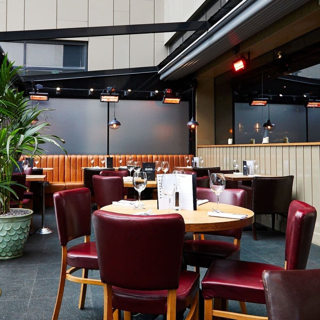 Blackhouse_Elegant_Dining_Setup_Wine_Glasses_Modern_Interior Elegant dining area at Blackhouse with leather seating, wooden tables, and wine glasses set for service under warm pendant lighting.