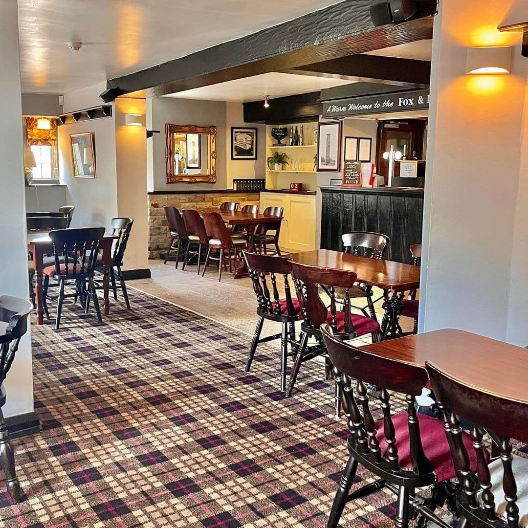 Fox and Hounds Cozy Pub Interior Wooden Furniture Plaid Carpet Interior of Fox & Hounds showing a cozy pub setting with wooden tables and chairs, patterned carpet, and warm lighting.