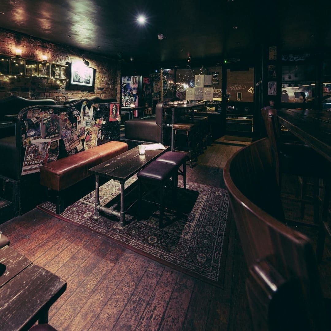 The East Village Cosy Retro Pub Interior Interior of a cozy bar in The East Village featuring eclectic decor, vintage posters, dim lighting, and comfortable seating with leather benches and wooden tables.