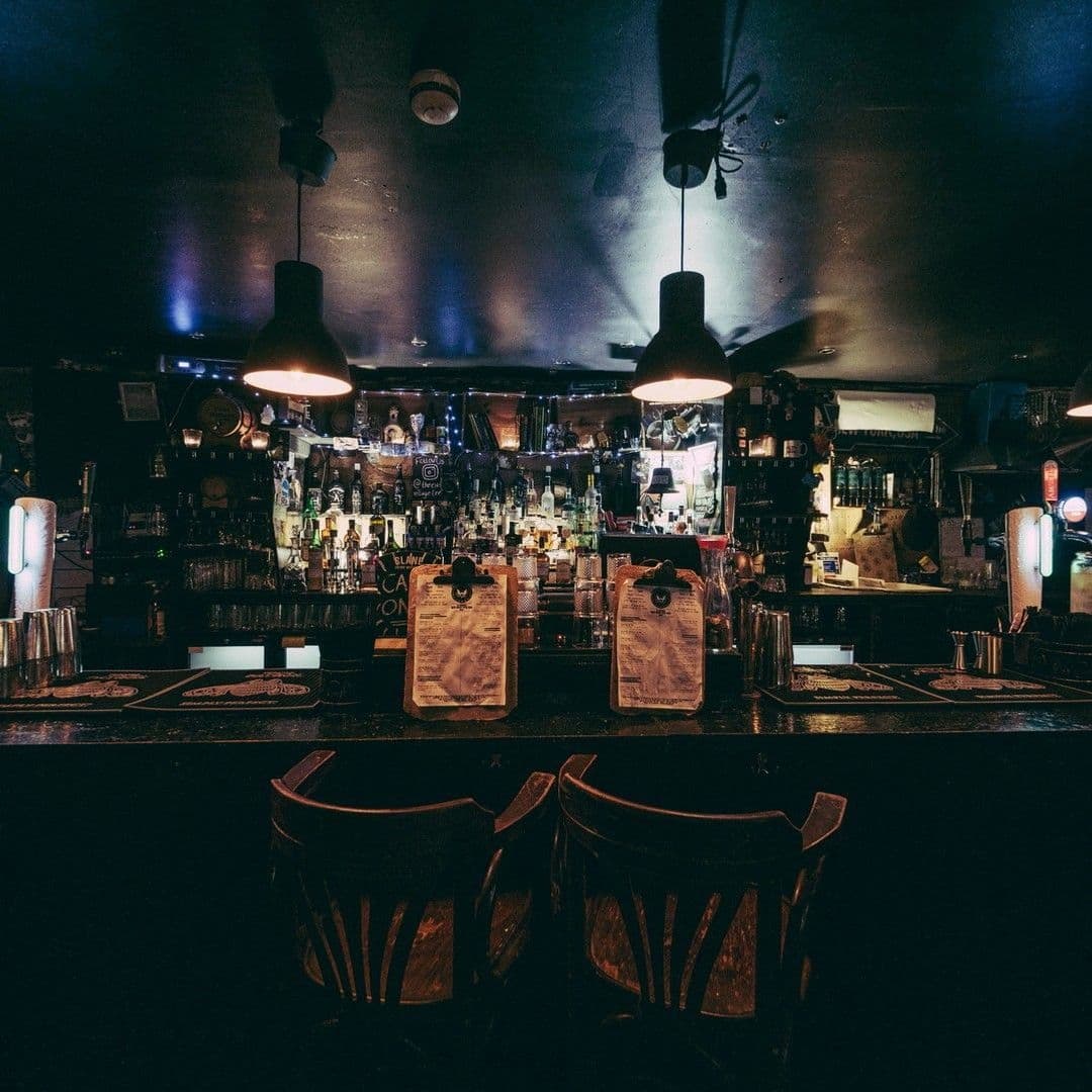 The East Village Cozy Pub Interior Nightlife Atmosphere Dimly lit bar interior in The East Village with wooden stools, a well-stocked bar counter, and hanging pendant lights.