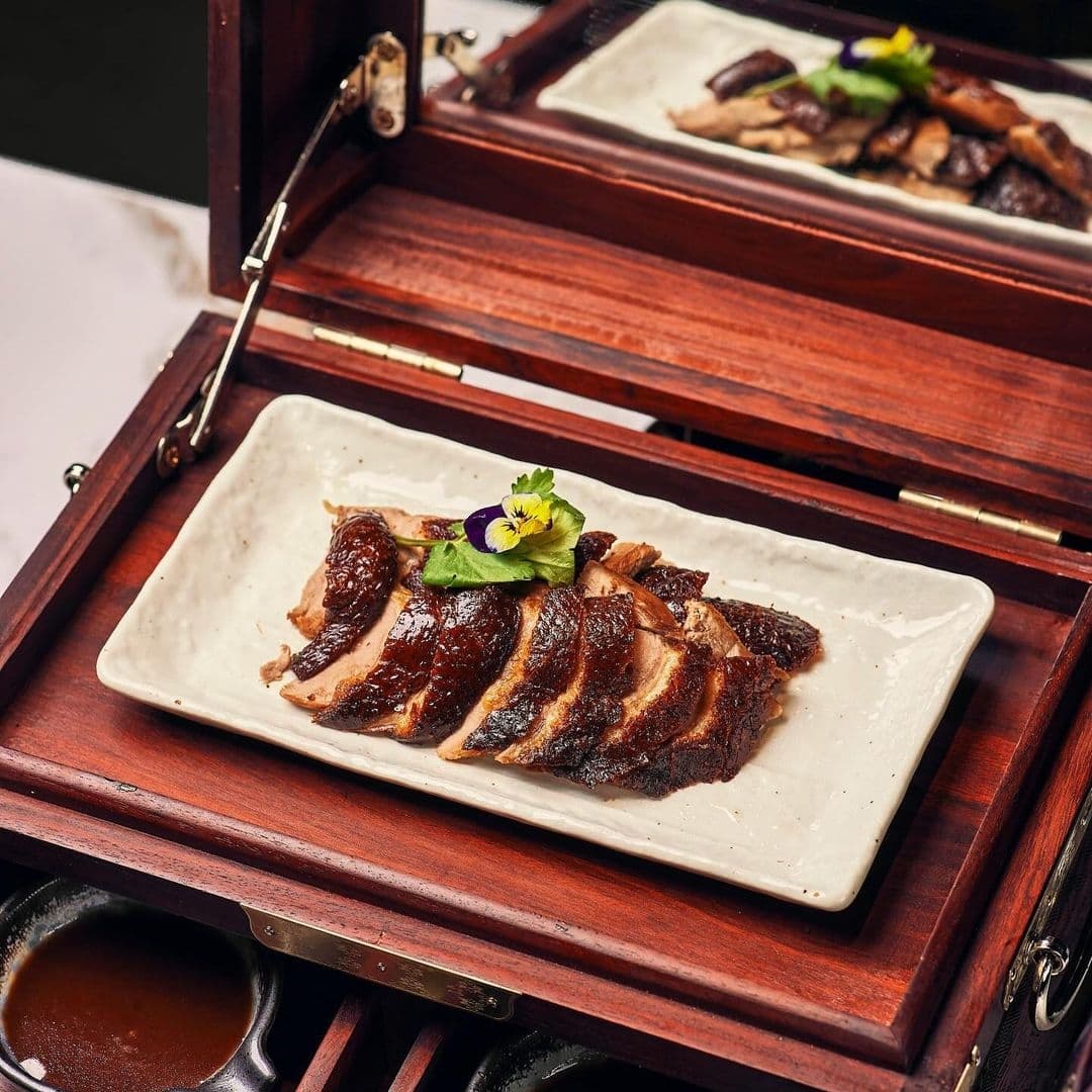 Blue Pavilion_Gourmet Duck Dish_Elegant Presentation Sliced roasted duck served on a white plate at Blue Pavilion, garnished with a purple edible flower, presented in an elegant wooden box.