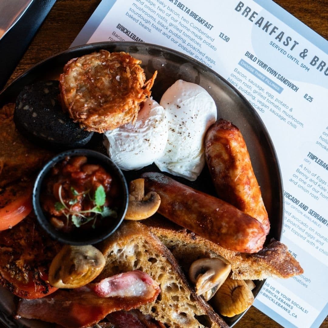 Bricklebanks Bar Kitchen Hearty English Breakfast Plate Traditional English breakfast served at Bricklebank's Bar & Kitchen, featuring poached eggs, sausages, bacon, grilled tomato, mushrooms, black pudding, hash browns, and toast with a side of baked beans.