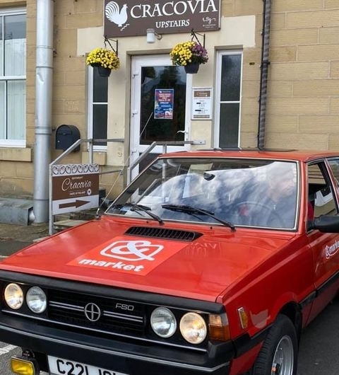 Cracovia Taste of Poland Vintage Car Entrance Red vintage car parked in front of Cracovia Taste of Poland restaurant with signage and flower baskets above the entrance.