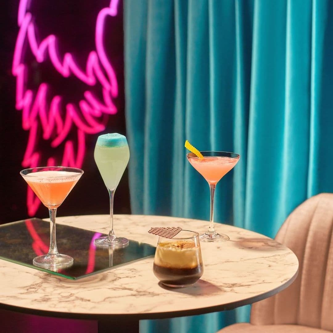 Dirty Martini_Cocktail Selection Neon Lights Elegant Decor Assorted colorful cocktails on a marble table at Dirty Martini, with a neon pink light and teal curtains in the background.