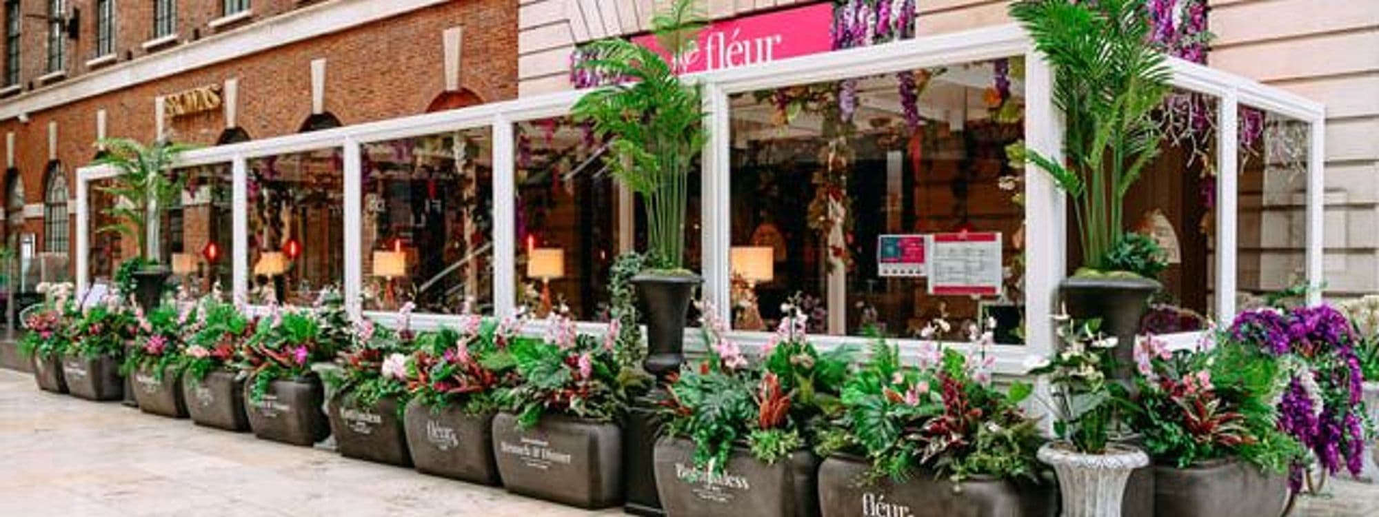 Exterior view of Fleur Restaurant and Bar with vibrant floral arrangements lining the front, large windows, and elegant outdoor seating visible.