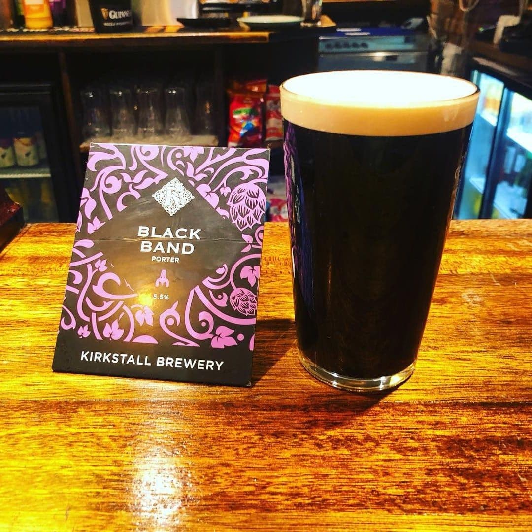 Fox and Grapes Porter Beer Kirkstall Brewery Bar Scene Pint of dark beer on a wooden bar counter with a promotional card for Black Band Porter by Kirkstall Brewery at Fox & Grapes.