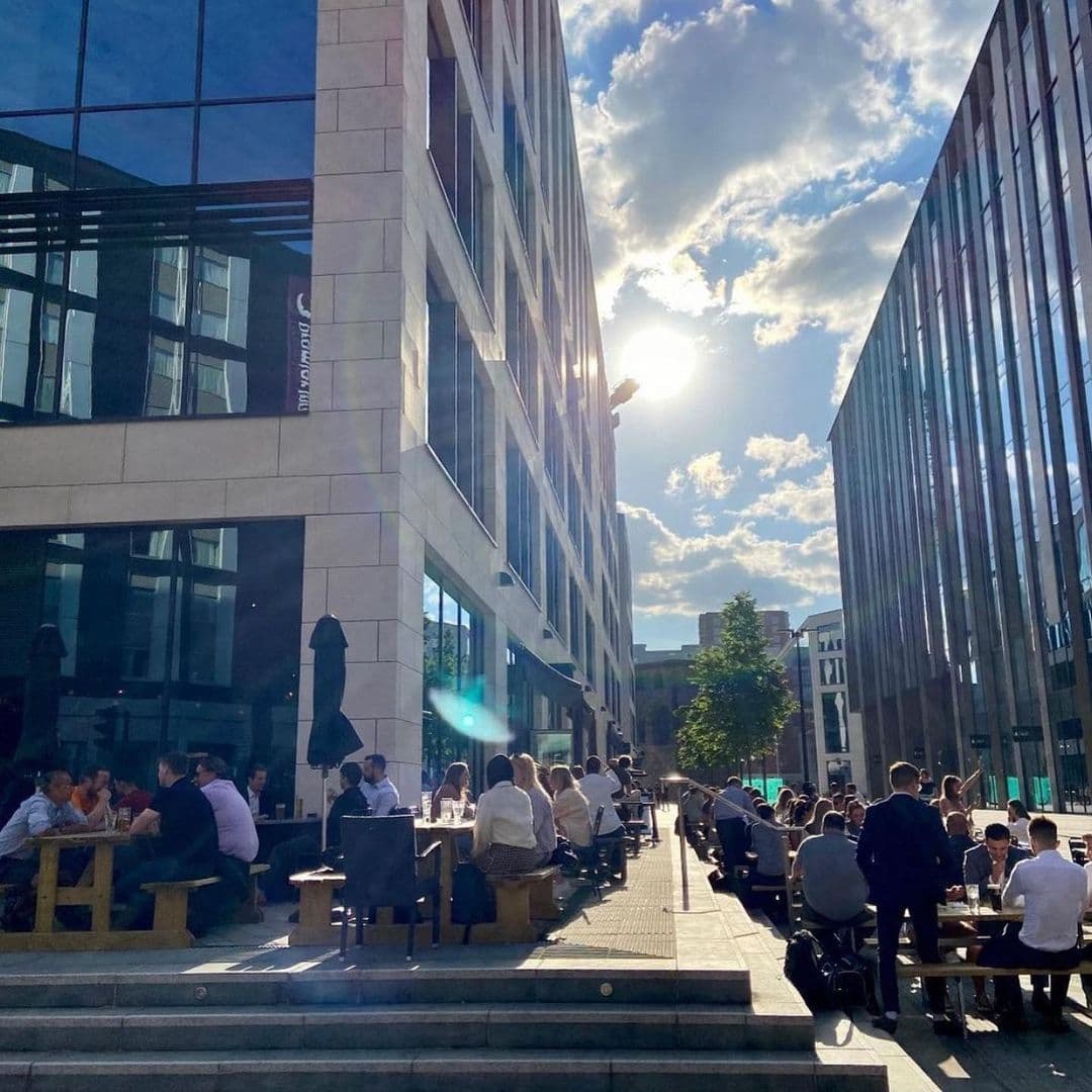 Hoist_House_Sunny_Outdoor_Gathering_Modern_Architecture Sunny day at Hoist House with people enjoying outdoor seating between modern buildings.