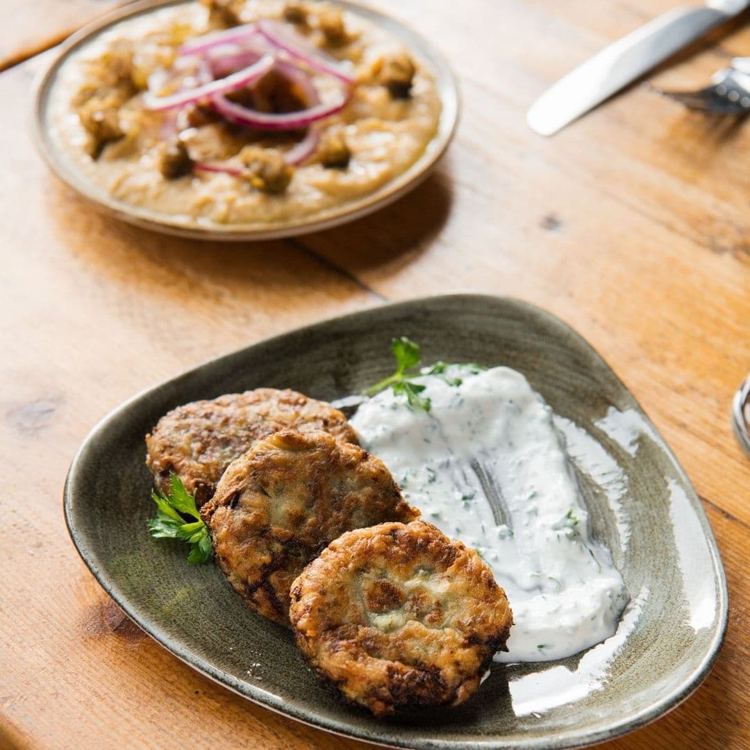 MYTHOS Chapel Allerton Greek Cuisine Appetizers Tzatziki Delicious Greek cuisine at MYTHOS Chapel Allerton, featuring a plate of golden-brown fried zucchini cakes served with a side of creamy tzatziki sauce, and a bowl of eggplant dip garnished with red onion slices in the background.
