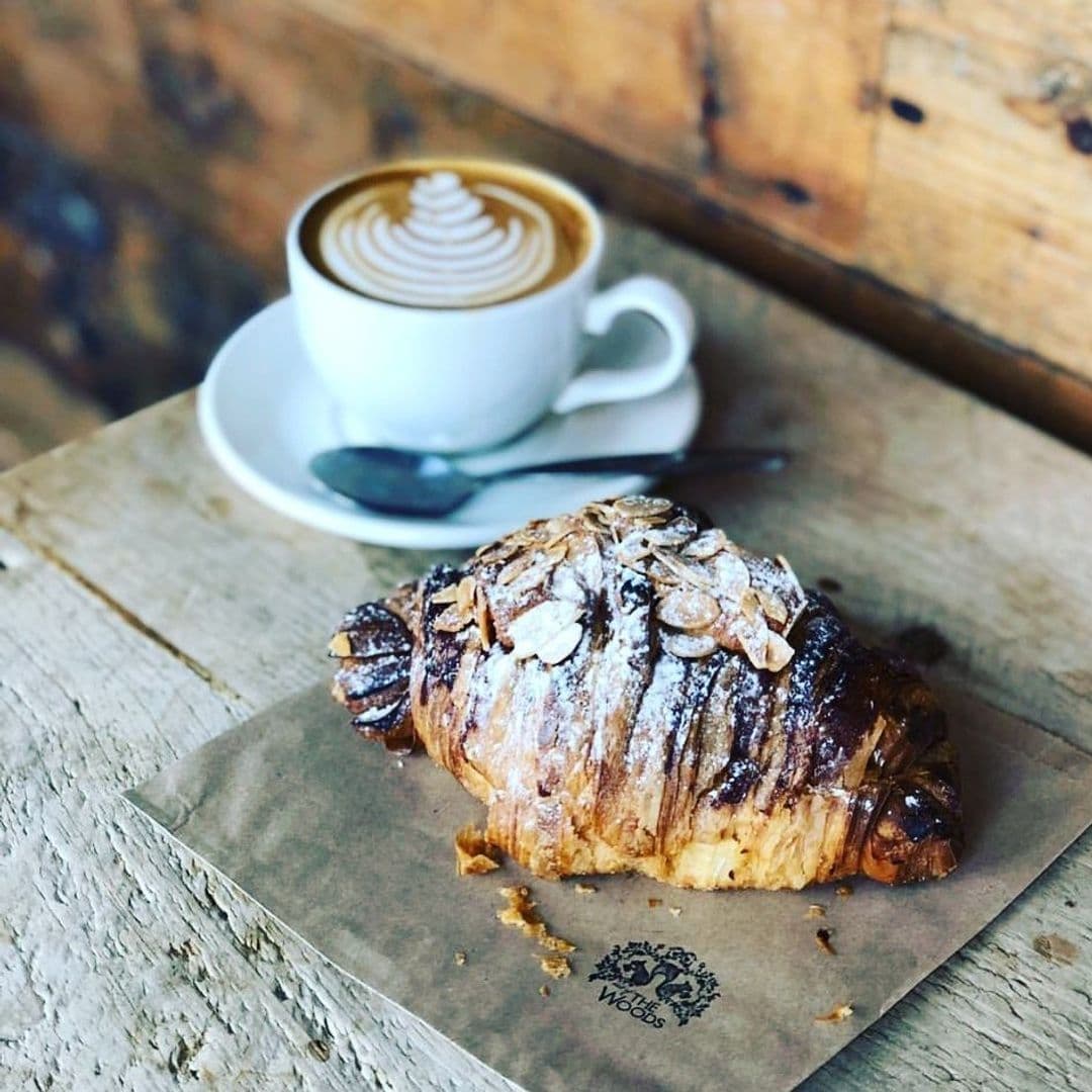Out of the Woods coffee croissant breakfast wooden table Freshly baked almond croissant and a cup of cappuccino with latte art on a rustic wooden table at Out of the Woods café.