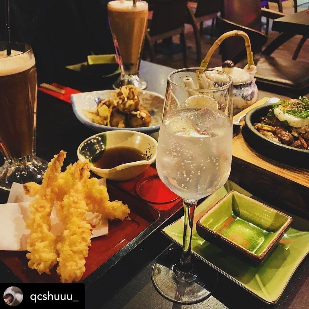 Sushi Waka Delicious Japanese Cuisine Dining Experience Dining table at Sushi Waka with a variety of Japanese dishes including tempura and grilled meats, accompanied by a glass of sparkling beverage and a creamy iced coffee.