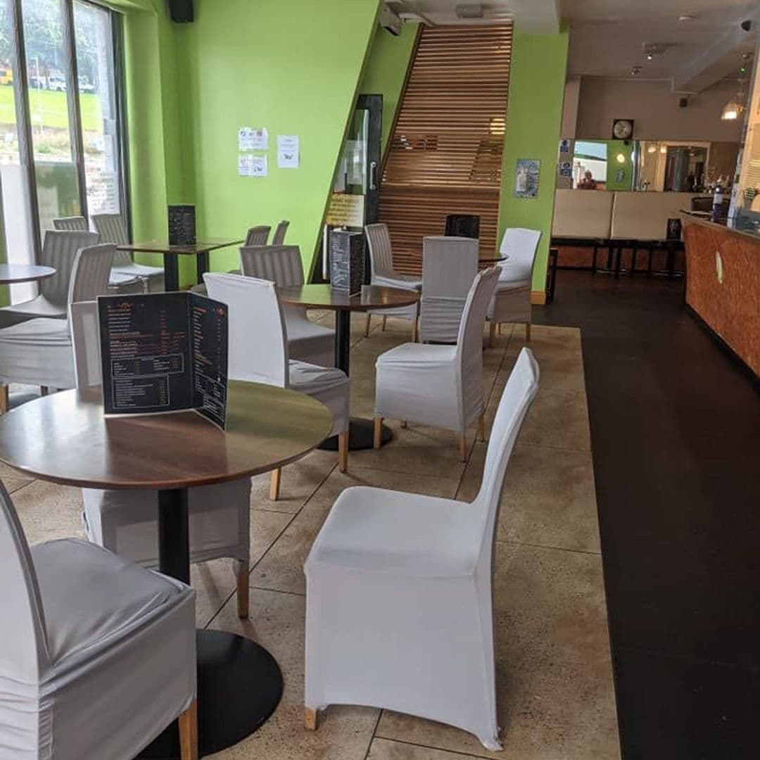 The Grand Valley Bar Kitchen Interior Modern Seating Area Interior view of The Grand Valley Bar & Kitchen featuring modern wooden tables with white chairs, bright green walls, and a well-lit bar area in the background.