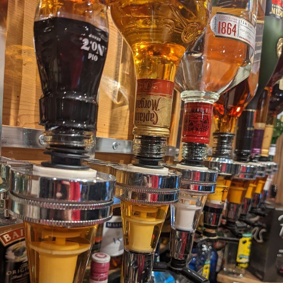 The Grand Valley Bar Kitchen Spirit Bottles Optics Display Optic spirit dispensers lined up at The Grand Valley Bar & Kitchen, showcasing a variety of alcoholic beverages.