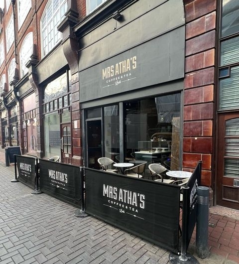 Mrs_Athas_Coffee_Shop_Exterior_City_Street Exterior view of Mrs Atha's coffee shop with outdoor seating behind black barriers featuring the cafe's name, set against a traditional red brick building.