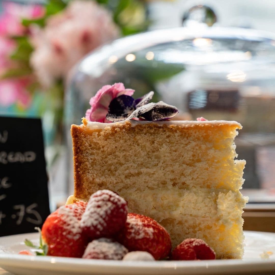 Olive Rye Delicious Cake Fresh Berries Decorated Dessert A slice of sponge cake garnished with powdered strawberries and a purple flower, on display at Olive & Rye.