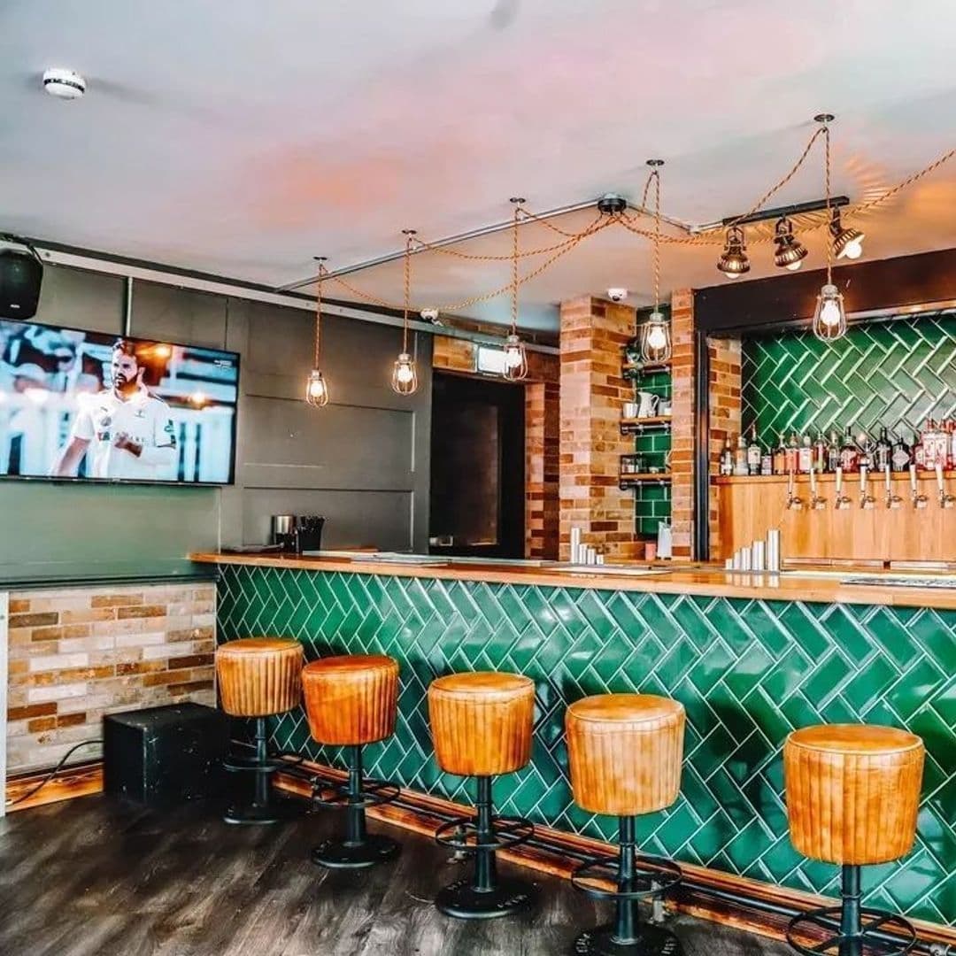 Parkside Tavern Modern Bar Interior Design Wooden Stools Interior of Parkside Tavern with a stylish bar counter, wooden stools, and hanging industrial lights, with a sports game on the television screen.