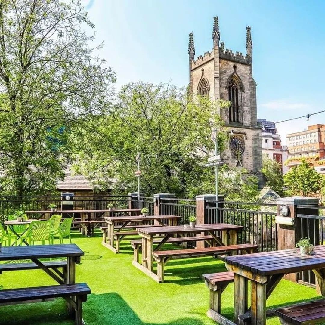 Parkside Tavern Outdoor Seating Historic Church View Outdoor seating area at Parkside Tavern with wooden benches, green chairs, and a view of a historic church tower in the background.
