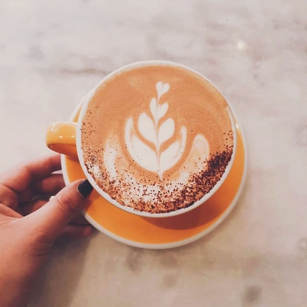 Wolfox_Coffee_at_ZAVIYA_Barista_Art_Latte_Handcrafted A hand holding a yellow cup of cappuccino with a beautiful latte art design on top, served on a matching saucer at Wolfox Coffee at ZAVIYA COFFEE Bar & Restaurant.