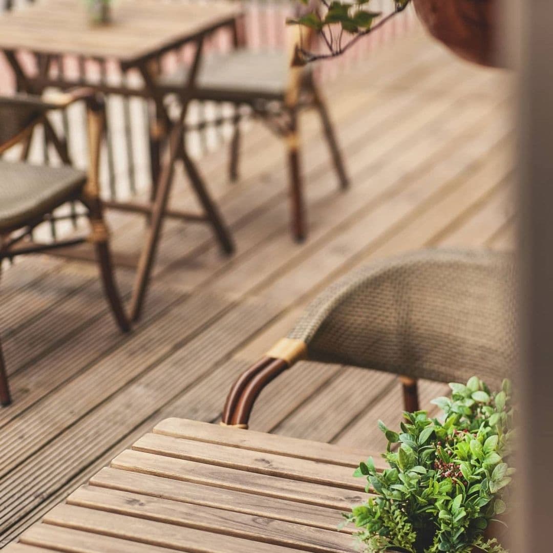Wolfox_Coffee_at_ZAVIYA_Coffee_Bar_Restaurant_Outdoor_Seating_Ambience Outdoor seating area at Wolfox Coffee at ZAVIYA COFFEE Bar & Restaurant featuring wooden tables and chairs on a deck with green plants.