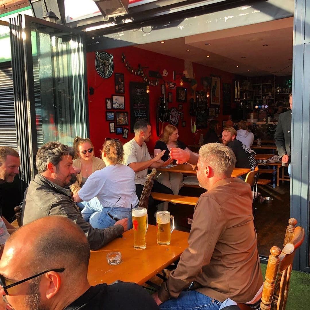 Alley Cats Cafe Bar Music Emporium Patrons Enjoying Drinks Sunny Afternoon Patrons enjoying drinks and conversation on the outdoor seating of Alley Cats Cafe Bar & Music Emporium, with a view into the vibrant red interior.