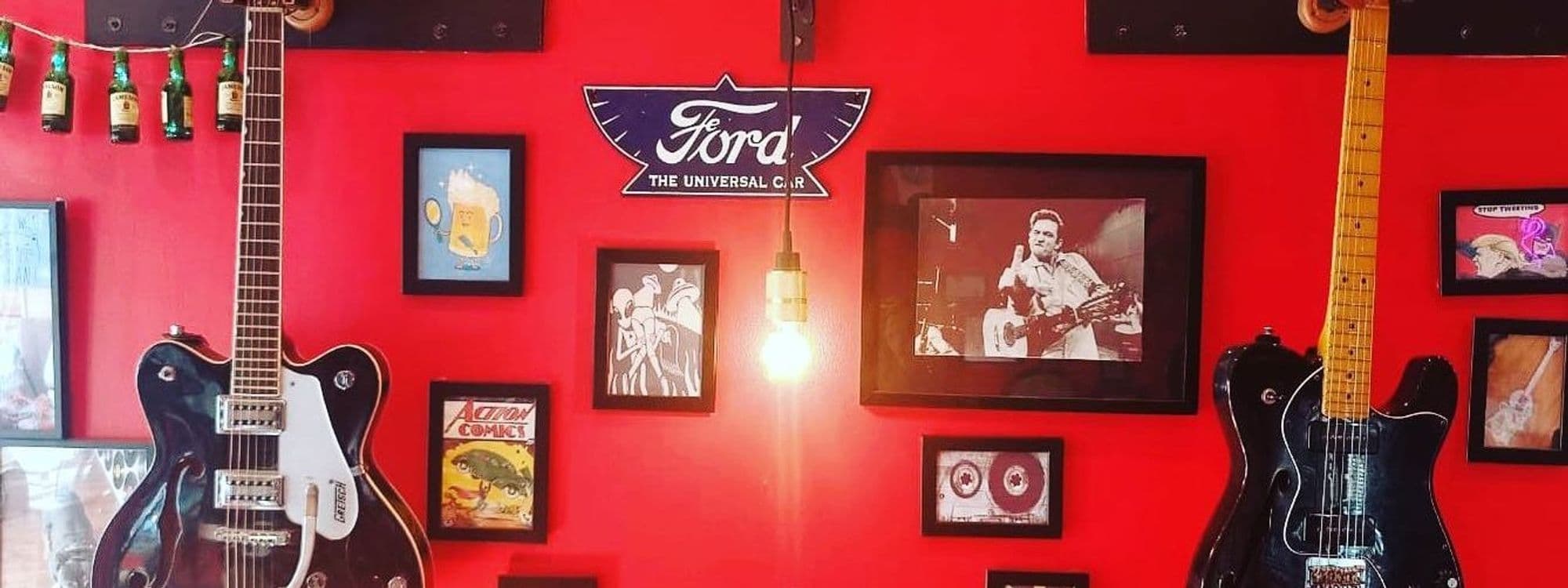 Interior of Alley Cats Cafe Bar & Music Emporium featuring a vibrant red wall adorned with guitars, framed pictures, and vintage posters.