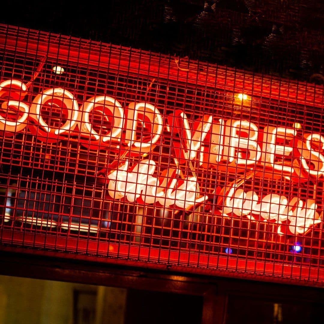 Be At One Boar Lane Good Vibes Neon Sign Red Amiance Neon sign reading "GOOD VIBES" behind a metal grid at Be At One – Boar Lane.