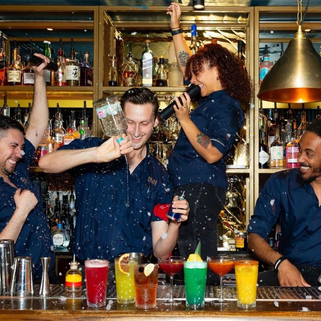 Be At One Boar Lane Vibrant Cocktail Making Fun Staff Vibrant atmosphere at Be At One – Boar Lane with smiling bartenders pouring and mixing colorful cocktails behind the bar.