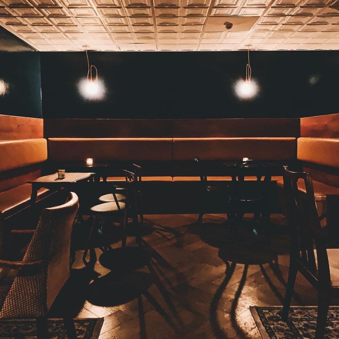 Below Stairs_Intimate Ambiance Dim Lighting Booth Seating Interior of Below Stairs with dim lighting, featuring cozy orange booth seating, pendant lights, and patterned floor rugs.