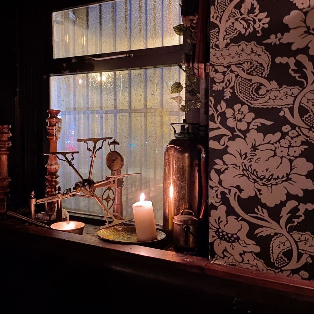 Blind Tyger Vintage Candlelight Decor Cozy interior corner at Blind Tyger with lit candles, vintage decor, and patterned wallpaper, creating an inviting and warm atmosphere.