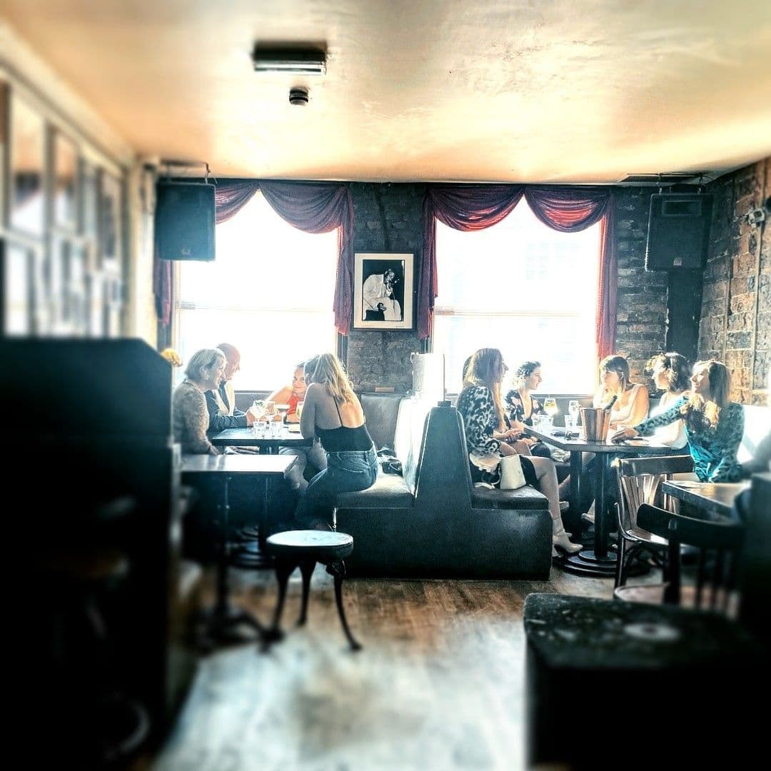 Blind_Tyger_Cozy_Ambiance_Social_Gathering Patrons socializing in the cozy, vintage-styled interior of Blind Tyger, with exposed brick walls and soft lighting.