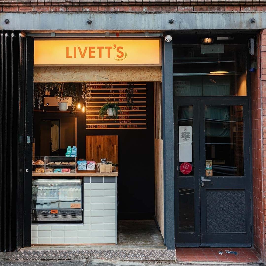 Livetts Coffee Shop Entrance Cozy Atmosphere Warm Lighting Entrance of Livett's Coffee Shop with illuminated sign, menu board, and display case with pastries.