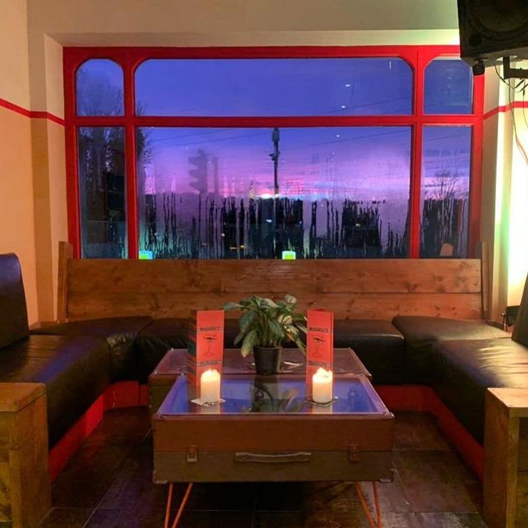 Melodie71_CozyEvening_AmbientLighting_WoodenFurniture Cozy interior of Melodie 71 with comfortable seating, wooden tables, lit candles, and large windows showing a twilight sky.