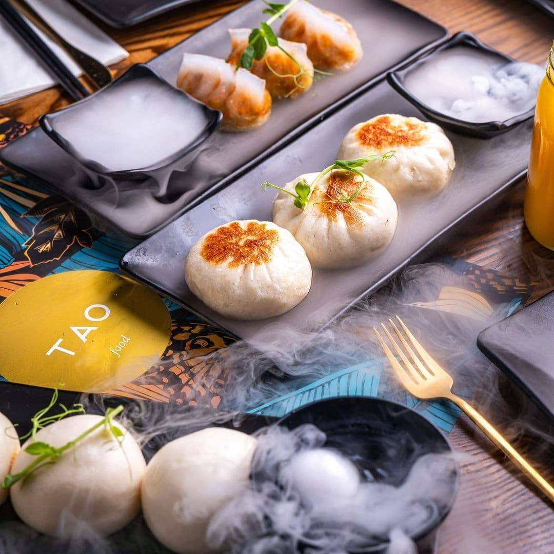 TAO_Gourmet_Asian_Cuisine_Dimsum_Dramatic_Presentation Gourmet dim sum and bao buns served at TAO restaurant, presented on elegant black plates with dry ice smoke for dramatic effect.