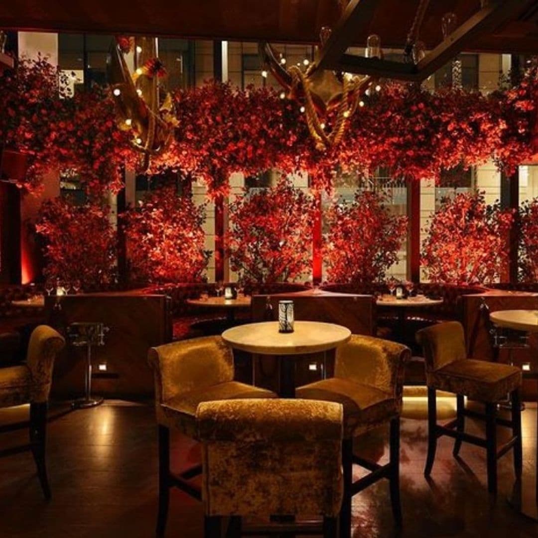 Tattu_AutumnAmbience_LuxuryDining_ElegantDecor Elegant dining area at Tattu with plush velvet chairs, wooden tables, and vibrant red foliage decor hanging from the ceiling.
