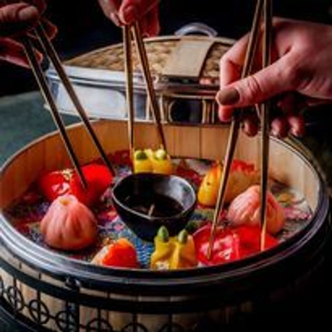 Tattu_DimSum_Platter_Colorful_Elegant Dim sum selection in a traditional bamboo steamer at Tattu restaurant with a person using chopsticks to pick up a dumpling.