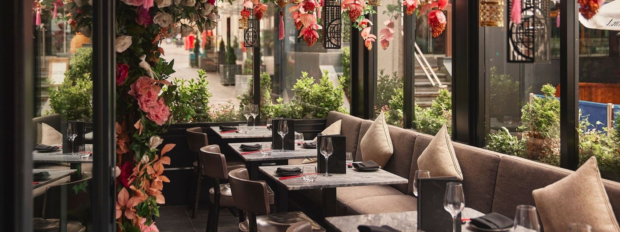 Elegant dining setup at Tattu with plush seating, marble tables, and vibrant floral decorations, offering a sophisticated and inviting atmosphere.