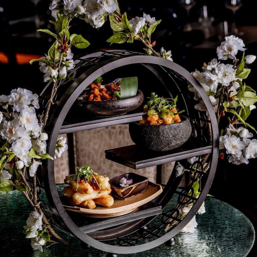 Tattu_Elegant_Presentation_Gourmet_Dishes Elegant gourmet dishes presented on a multi-tiered circular stand adorned with white blossoms at Tattu restaurant.